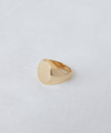 The Gemma Signet Ring in 14k gold, featuring a smooth, round, flat top, is shown on a white textured fabric background.