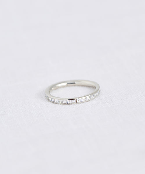 The Iris Eternity Band, inspired by Jenni Kayne, features small clear stones set in a delicate white gold band and is beautifully displayed on a white textured surface.