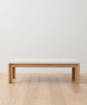 The Otto Bench, featuring a natural linen seat, stands on a wooden floor against a plain white wall.