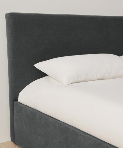 The Pacific Bed features an upholstered headboard and a white pillow, crafted from elegant Belgian linen.