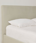 A close-up of the Pacific Bed features a light beige Belgian linen upholstered headboard, white pillow, and crisp white bedding set against a plain white wall.